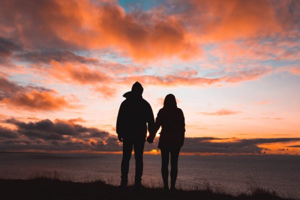 silhouette photo of man and woman on cliff